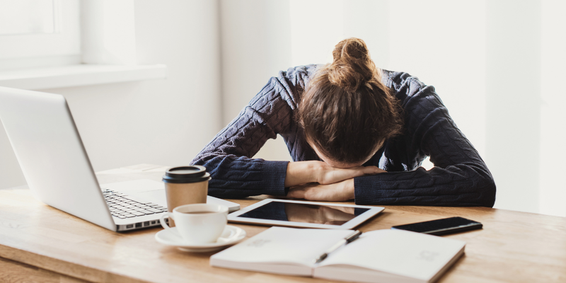 Woman with her head down at her desk in front of her computer.