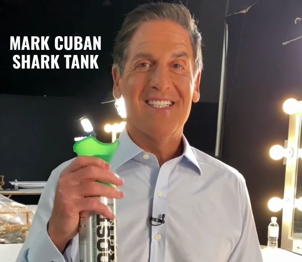 Mark Cuban holding a can of Boost Oxygen, in front of a dark studio background with a lighted vanity mirror visible on the right. Text on the top left reads 'MARK CUBAN SHARK TANK'.