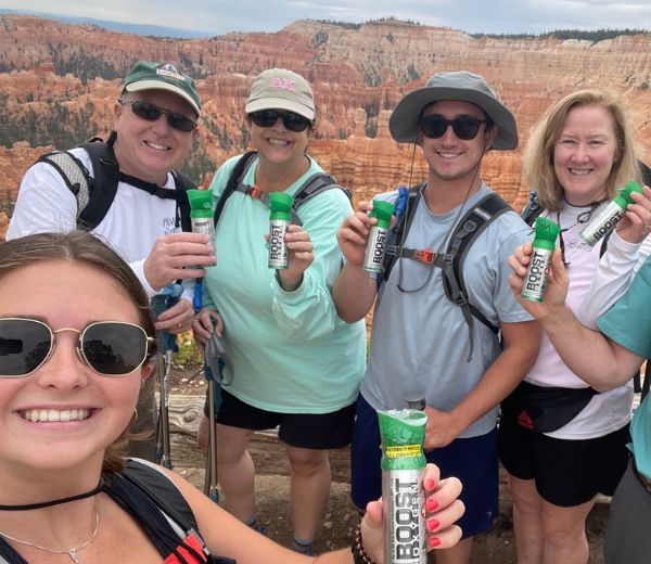 A group of hikers taking a selfie outdoors in a canyon setting, each holding a Boost Protein canister.