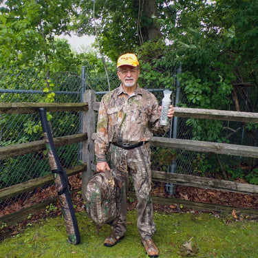Hunter is his hunting gear with his backpack and gun holding a can of Boost Oxygen Outdoors.