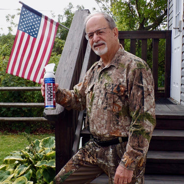Older man in camo gear in front of steps holding a can of Boost Oxygen Stars and Stripes with an American flag in the background.