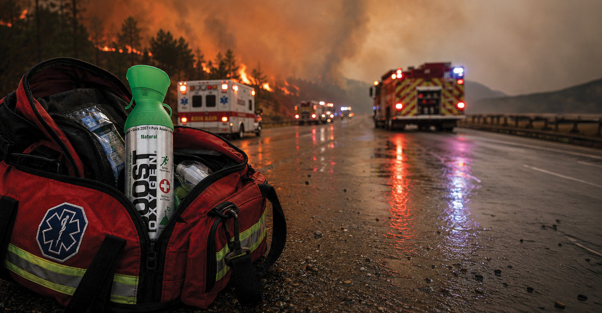 A Boost Oxygen canister sits in a emergency personnel bag on a road with a forest fire and emergency vehicles in the background.