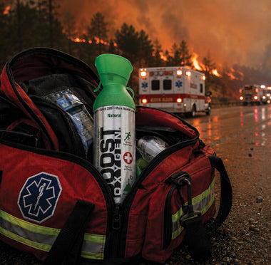 A Boost Oxygen canister sits in a emergency personnel bag on a road with a forest fire and emergency vehicles in the background.